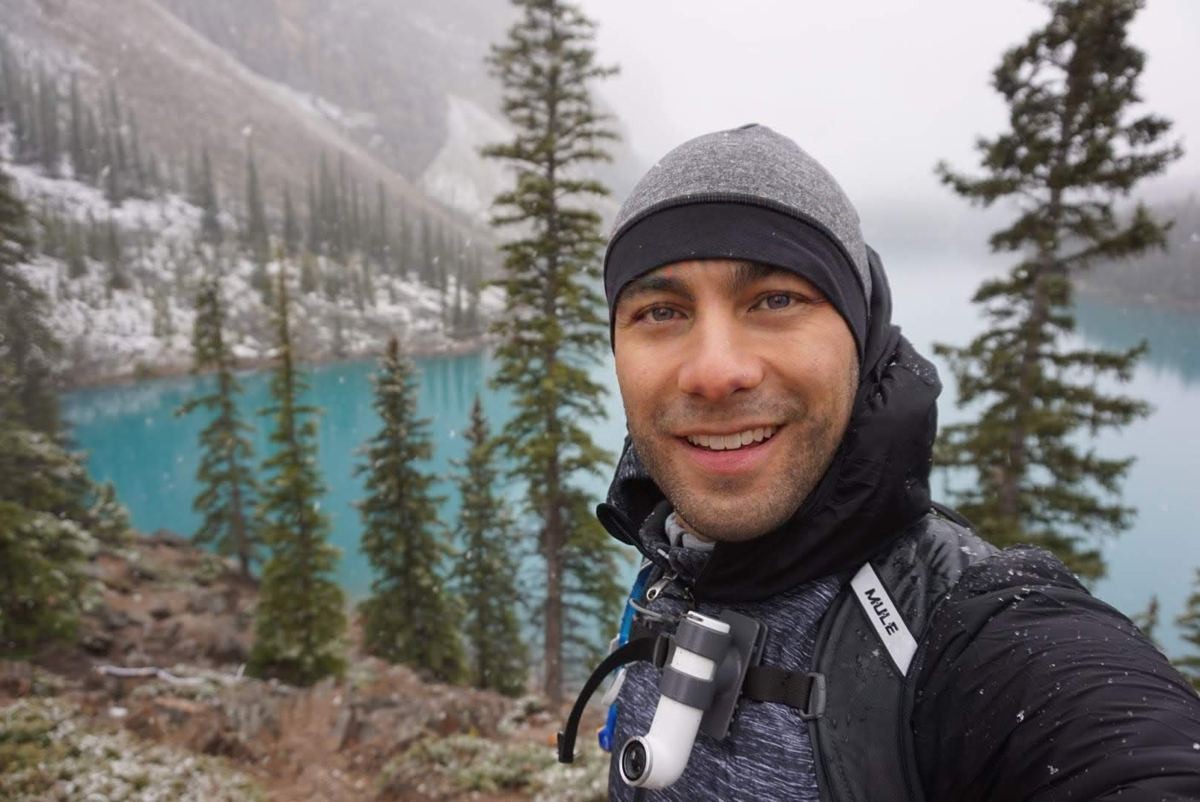 Manny taking a selfie in a beanie beside a turquoise mountain lake in light snow